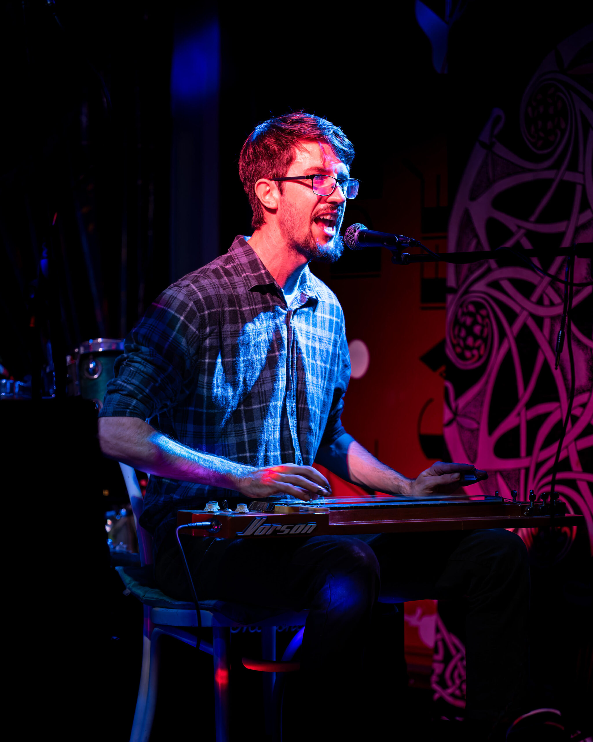 Taipan Tuckey performing live on stage, singing and playing slide guitar under coloured stage lights